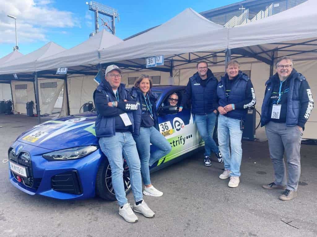 Gruppe von Menschen neben einem blauen Elektroauto bei einem Event.