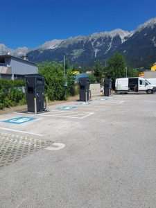 Ladestation für Elektroautos in einer Parkzone mit Bergen im Hintergrund.