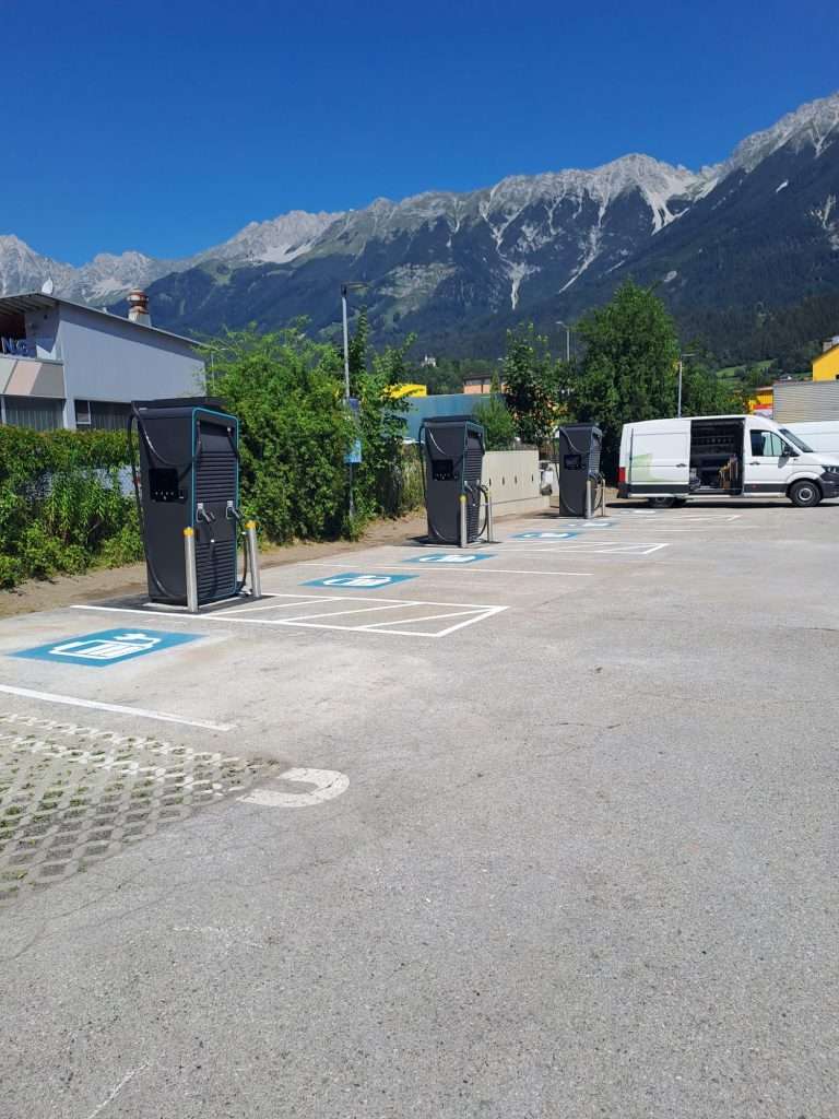 Ladestation für Elektroautos in einer Parkzone mit Bergen im Hintergrund.